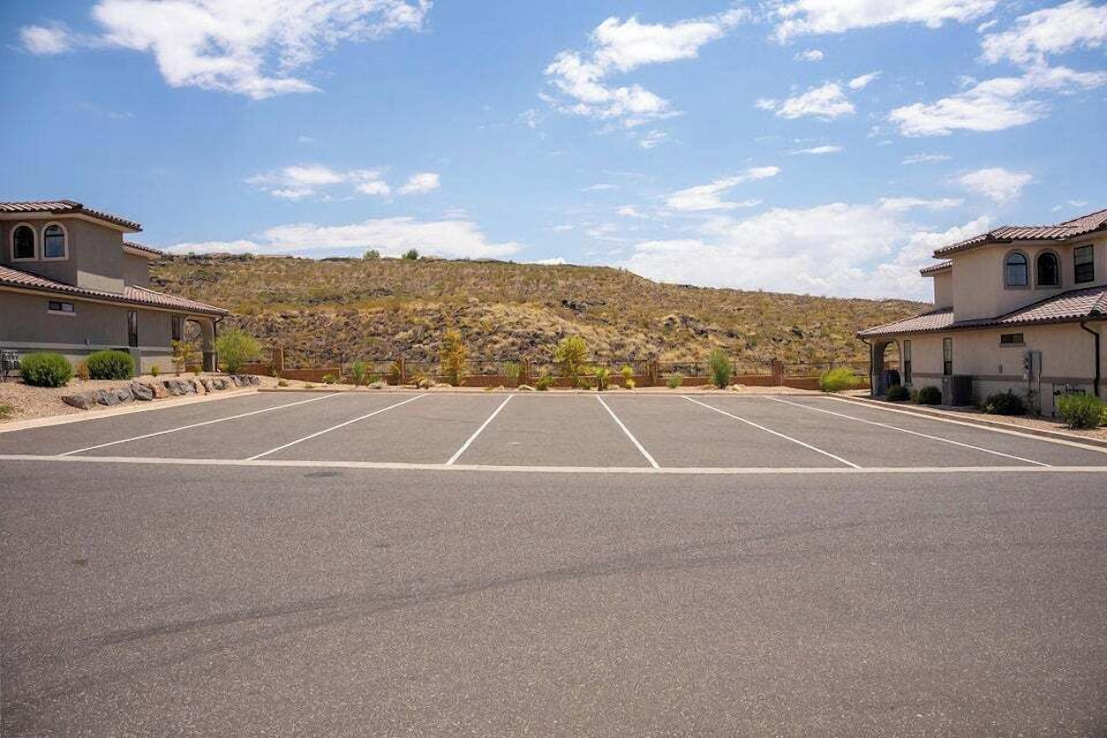 A parking lot with multiple spaces, a building with a tiled roof, and a hilly landscape in the background.