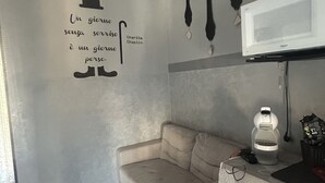 A modern kitchen with a beige sofa, a microwave, and a wall with cutlery and a quote. - Nicuzza House (Avola)