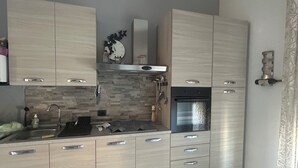 A modern kitchen with light wood cabinets, a stainless steel oven, and a tiled backsplash. - Nicuzza House (Avola)