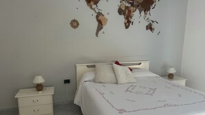 A neatly arranged bedroom with a world map on the wall, a bed with white bedding, two bedside tables with lamps, and a small drawer unit. - Nicuzza House (Avola)