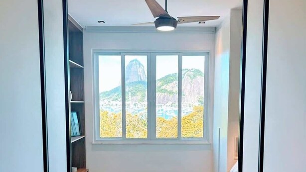 A bedroom with a bed, a ceiling fan, and a large window with a view of a mountain and cityscape.