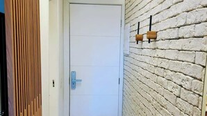 A hallway with a white door, a wooden slatted partition, and a brick wall with two wall-mounted light fixtures.