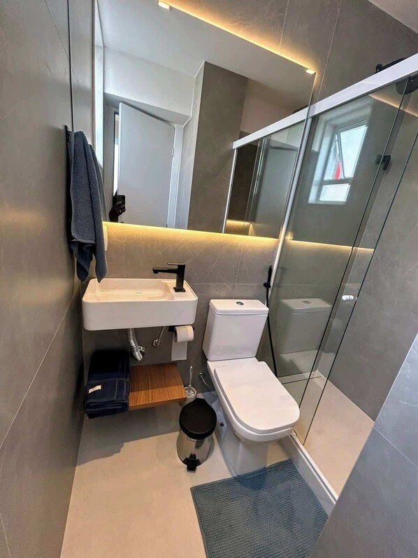 Un baño moderno con cabina de ducha de vidrio, inodoro y lavamanos con una toalla colgada en la pared.