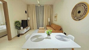A modern living room with a white dining table, beige sofa, and a TV on a stand. - OYO HOME 1405 Spacious 1bed In Jvc Be (Dubai)