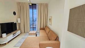 A modern living room with a large flat-screen TV, beige curtains, a sofa, and a city view through the window. - OYO HOME 1405 Spacious 1bed In Jvc Be (Dubai)