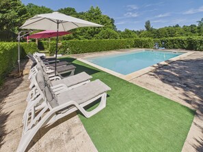 A swimming pool with a green artificial lawn, lounge chairs, and a large umbrella.