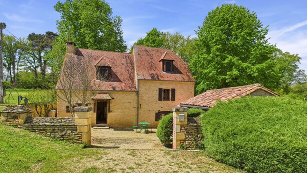 A two-story stone house with a tiled roof, a stone entrance, and a gravel driveway.