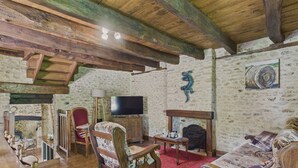 A rustic living room with wooden beams, a fireplace, a television, and vintage furniture.