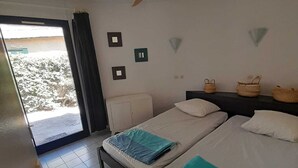 A hotel room with two beds, a ceiling fan, a view through a glass door, and a small table. - Fisherman's farmhouse between the swimming pool, the Etang de Salses-Leucate and the Mediterranean (Le Barcarès)