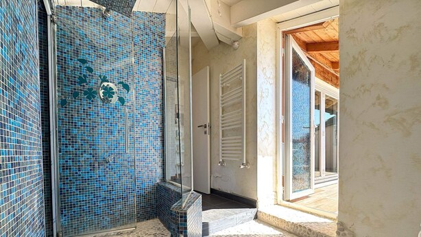 A bathroom with mosaic tile walls, a shower area, and a stone floor. - Penthouse Bay View (Sestri Levante)