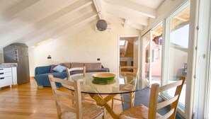 A spacious living area with a glass-top dining table surrounded by wooden chairs, a sofa, and a kitchen area with a refrigerator and cabinets. - Penthouse Bay View (Sestri Levante)