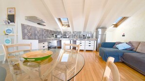 A modern kitchen with a glass dining table, wooden chairs, and a blue sofa in a loft-style living area. - Penthouse Bay View (Sestri Levante)