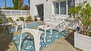 An outdoor patio area with white furniture, a patterned rug, and potted plants.