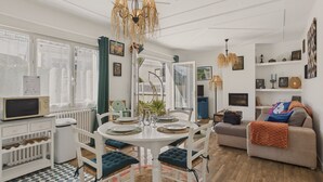 A modern living room with a dining area, white furniture, a patterned rug, and a wooden floor.