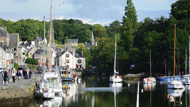 A harbor with boats docked, a church, and a crowd of people walking along the waterfront.