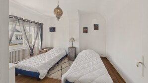 A bedroom with two beds, a radiator, a window with curtains, and a hanging light fixture.