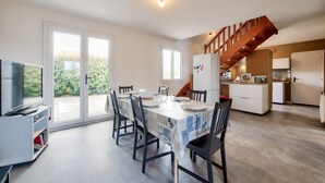 Un vaste espace de salle à manger avec une table dressée pour quatre personnes, une cuisine en arrière-plan et un escalier menant à l’étage supérieur.