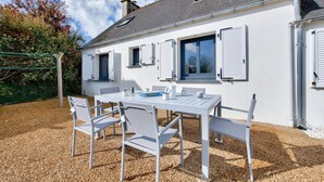 Un bâtiment blanc avec des volets, une table avec des chaises et un sol recouvert de gravier.