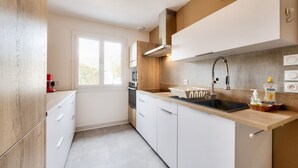 Une cuisine moderne avec des meubles blancs, un plan de travail en bois, un évier en acier inoxydable et une fenêtre qui laisse entrer la lumière naturelle.