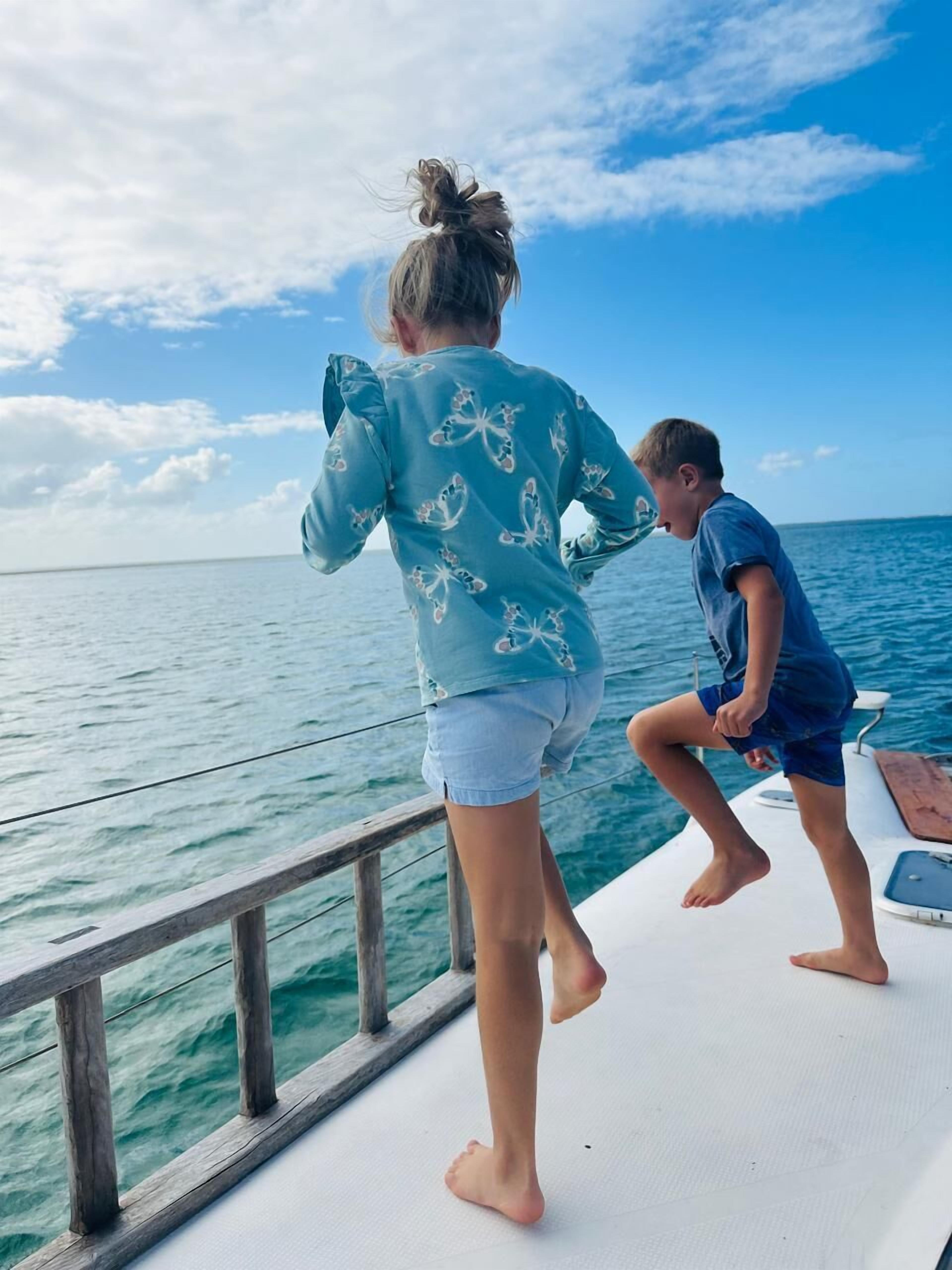 A boat with a wooden railing and a person in a blue shirt and denim shorts standing on the deck.