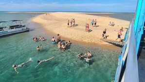 A beach with clear water, people swimming and sunbathing, and a boat docked nearby. - Golden Palms Beach Resort (Jangamo)