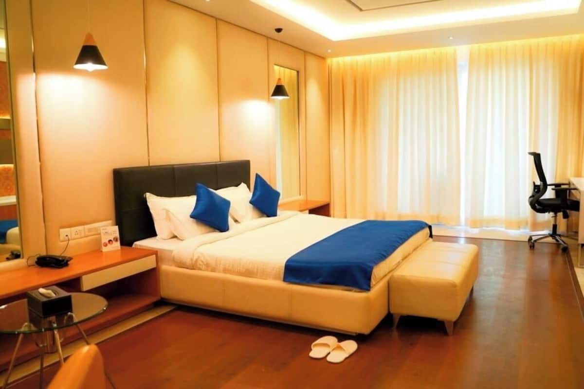 A modern hotel room with a large bed, a desk with a chair, a small table, and a treadmill.