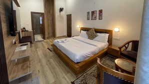 Een slaapkamer met een houten bed, nachtkastjes, een stoel en een kleine tafel. Er is een deur naar een andere kamer en een wandlamp.