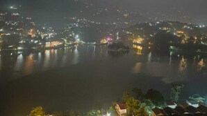Een nachtzicht van een stadsbeeld met een waterpartij voorop, verlichte gebouwen en een opvallende heuvel op de achtergrond.