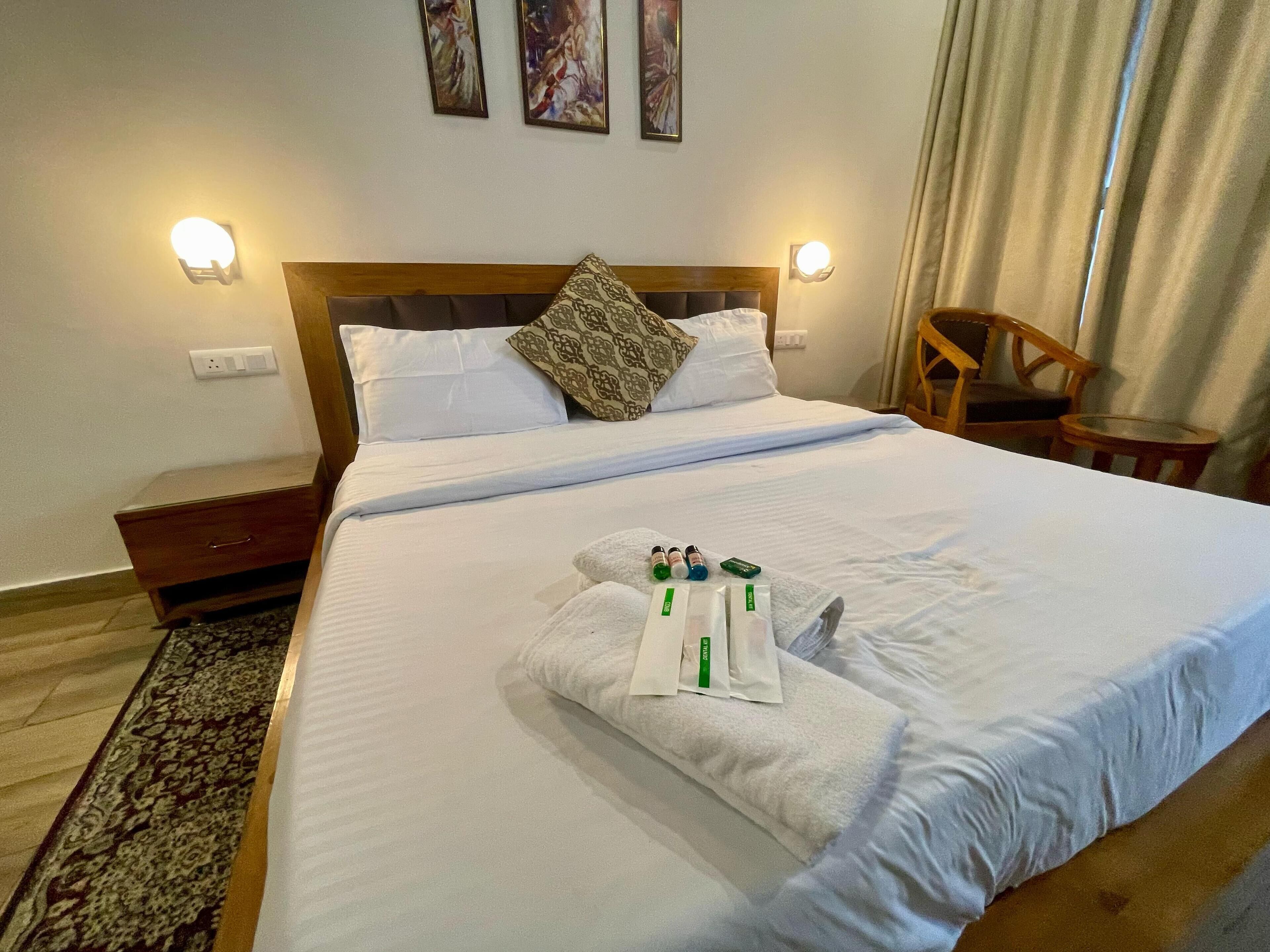 A neatly made bed with white linens, a wooden headboard, and a decorative pillow. There are two wall-mounted lights and a small wooden chair beside the bed.