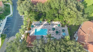 An aerial view of a resort with a swimming pool, lounge chairs, and palm trees.
