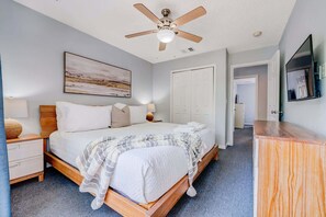 A bedroom with a bed, bedside tables, a ceiling fan, a painting, and a TV.