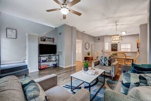 A spacious living room with a flat-screen TV, a ceiling fan, and a dining area with wooden chairs and a table. - Spacious 3BR retreat w/ pool access & park views (Kissimmee)