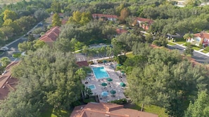 An aerial view of a residential area with a swimming pool surrounded by trees and houses. - Spacious 3BR retreat w/ pool access & park views (Kissimmee)