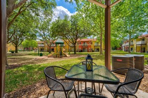 An outdoor patio with a table and chairs, a playground, and residential buildings in the background.