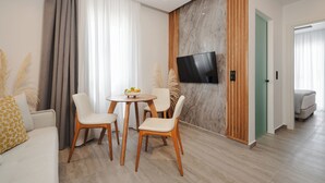 Una sala de estar moderna con un televisor de pantalla plana montado en una pared de mármol, una mesa redonda de madera con sillas y un sofá con almohadones decorativos.