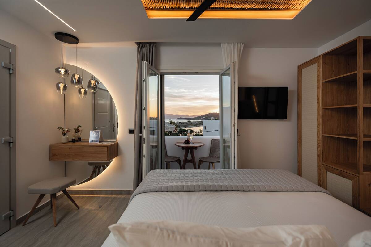 Une chambre d’hôtel moderne équipée d’un lit, d’un bureau avec une chaise, d’une petite table avec deux chaises, d’une télévision et offrant une vue sur le paysage urbain.