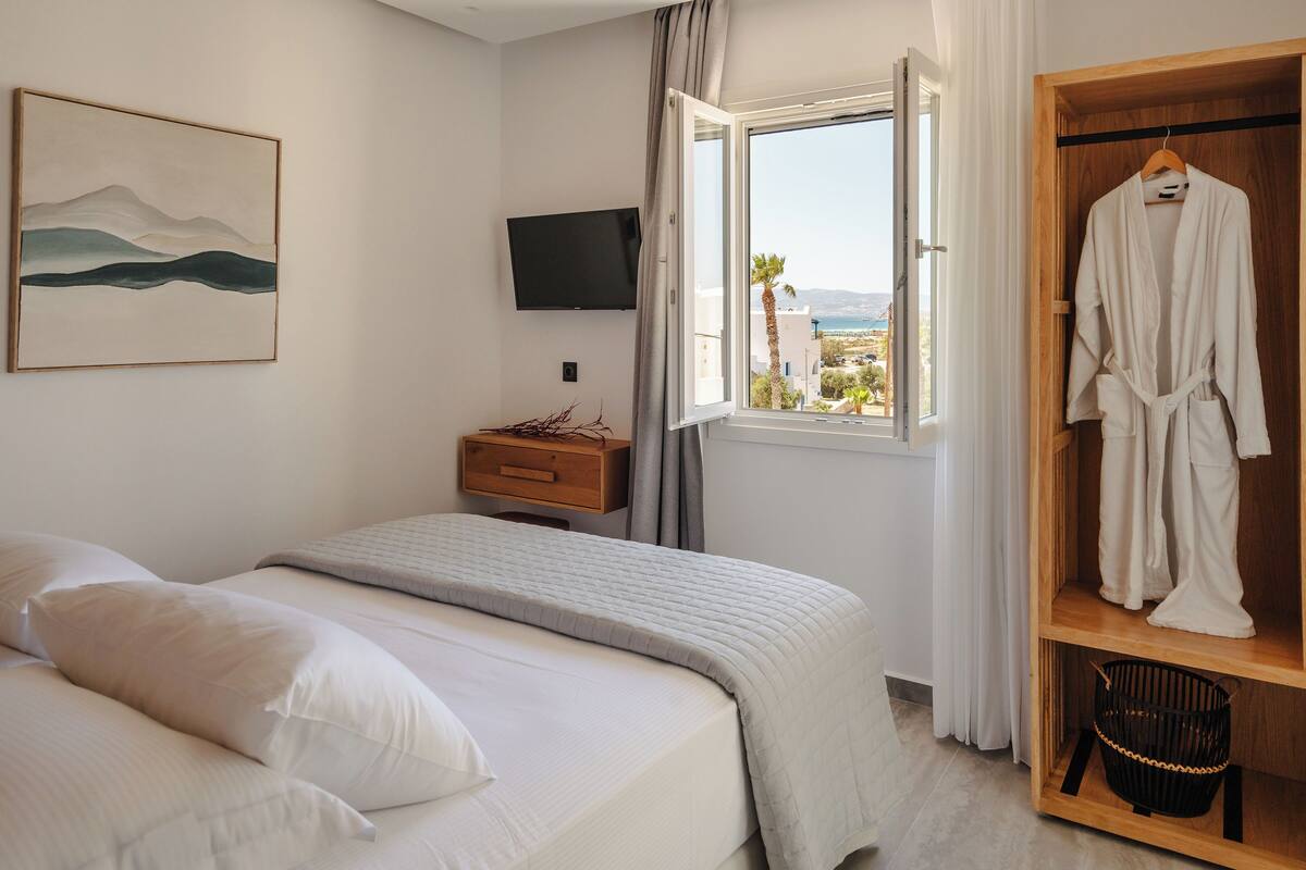 Une chambre à coucher avec un lit, une télévision, une fenêtre donnant sur un beau paysage et un peignoir suspendu à un porte-vêtements en bois.