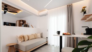 Una sala moderna con un sofá, una mesa redonda pequeña, una mesa de centro, un televisor y una zona de cocina con una cafetera.