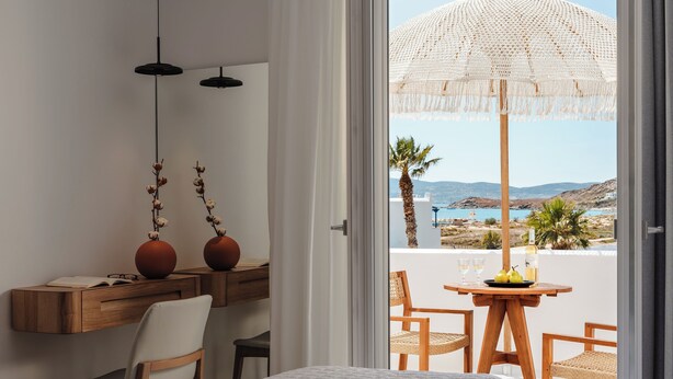 Un dormitorio con cama, escritorio y silla, y vista al mar desde un balcón.