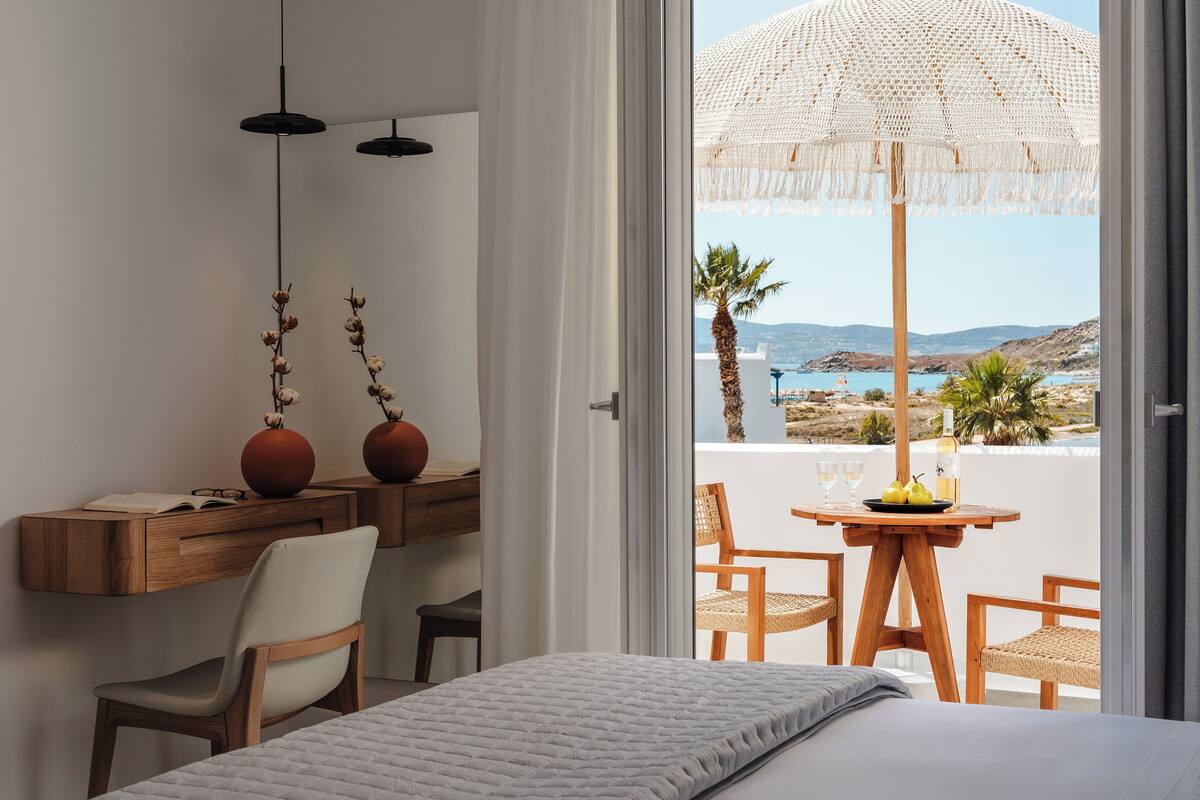 Une chambre avec un lit, un bureau et une chaise, et une vue sur la mer depuis un balcon.