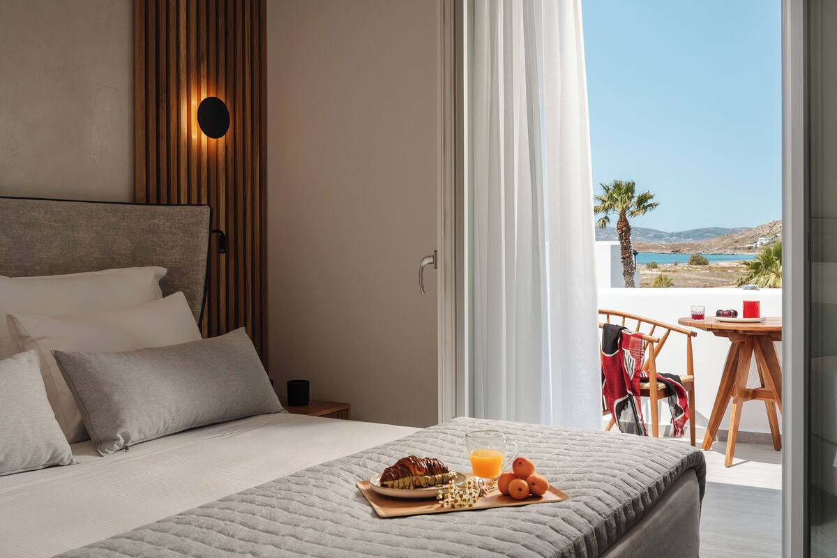 Une chambre d’hôtel avec un lit, un plateau de petit-déjeuner et un balcon équipé d’une table et de chaises.