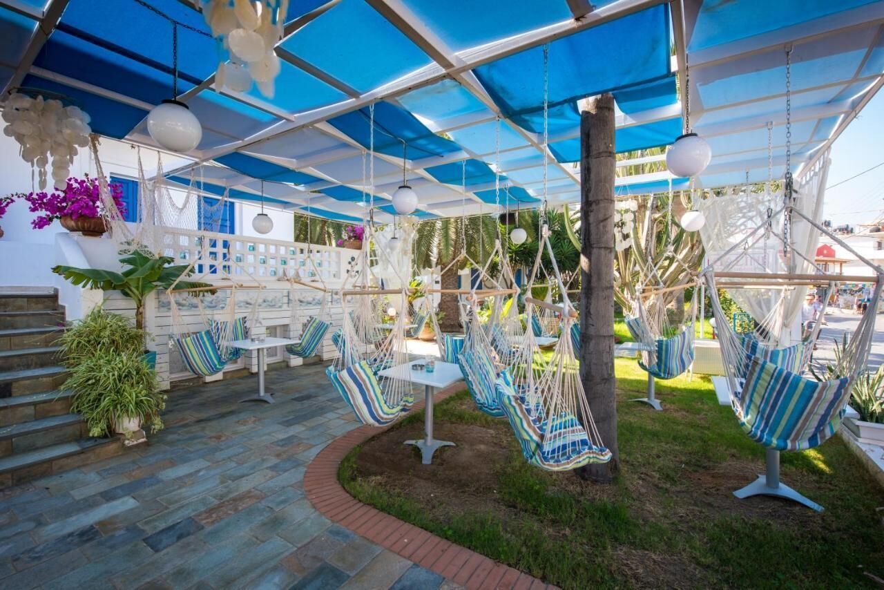 A covered outdoor seating area with hammocks and tables, surrounded by potted plants and a brick pathway.