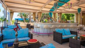 Een overdekt terras met rieten meubels, een bar en uitzicht op palmbomen.
