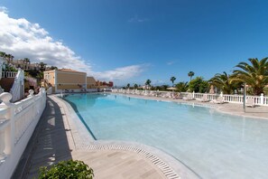 Ein großer Swimmingpool mit weißem Zaun und Liegestühlen, umgeben von Palmen und Gebäuden.