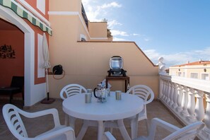 A balcony with a round table, white chairs, a coffee pot, and a television.