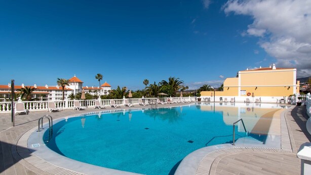 Una piscina con un deck de azulejos, sillones de descanso y un cielo azul despejado.