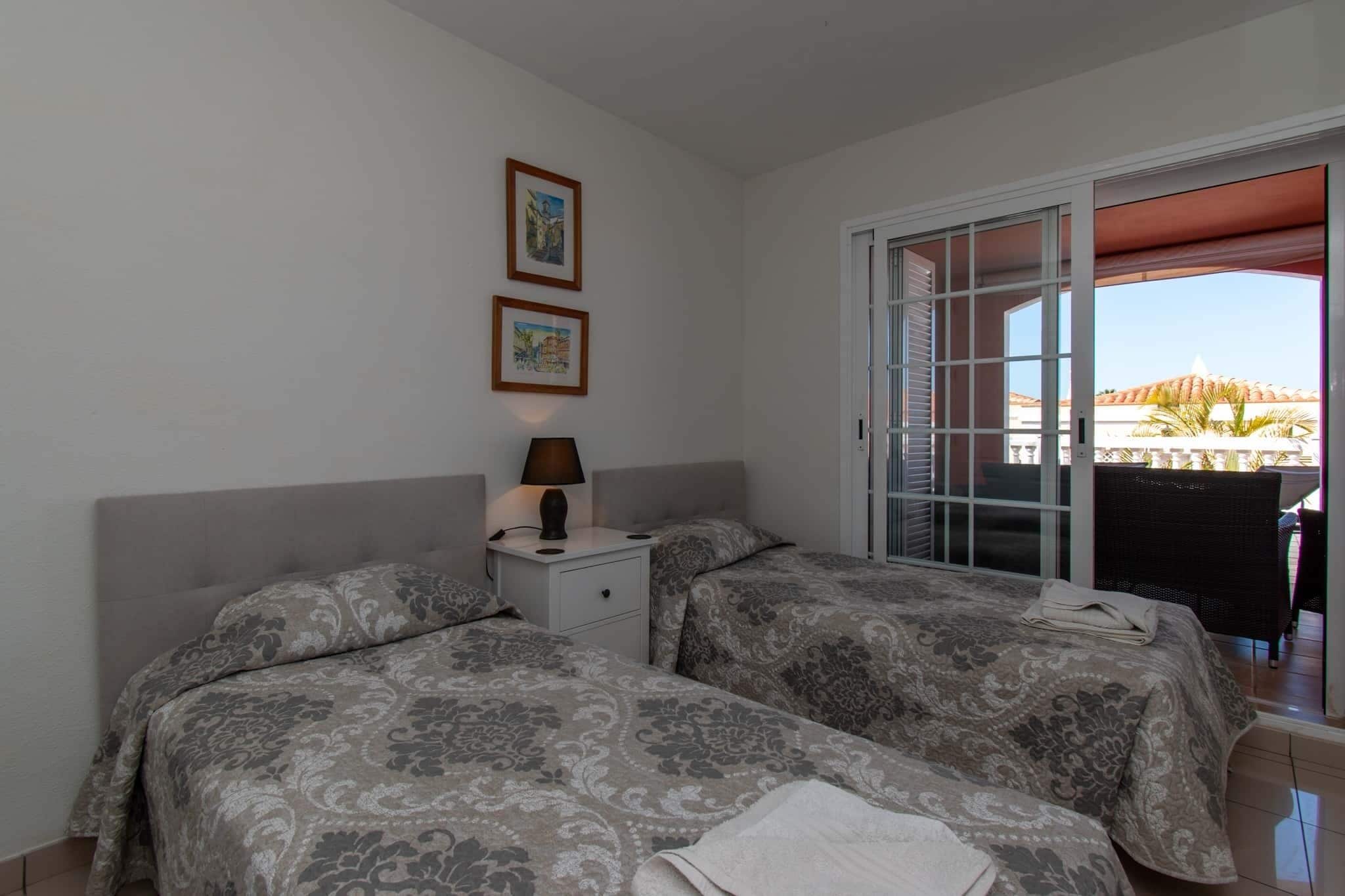 Habitació d'hotel amb dos llits, una taula de nit amb làmpada i una porta corredissa de vidre que dona a una zona exterior.