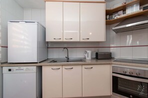 Uma cozinha com armários brancos, lava-louças, pia, torradeira e forno.