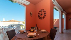 Un comedor con una mesa preparada para dos, un reloj de pared y vistas a un edificio con tejado de azulejos.