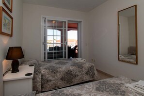 A bedroom with a bed, a bedside table with a lamp, a mirror, and a view of the outside. - El Veril del Duque 13 - Two Bed (Costa Adeje)